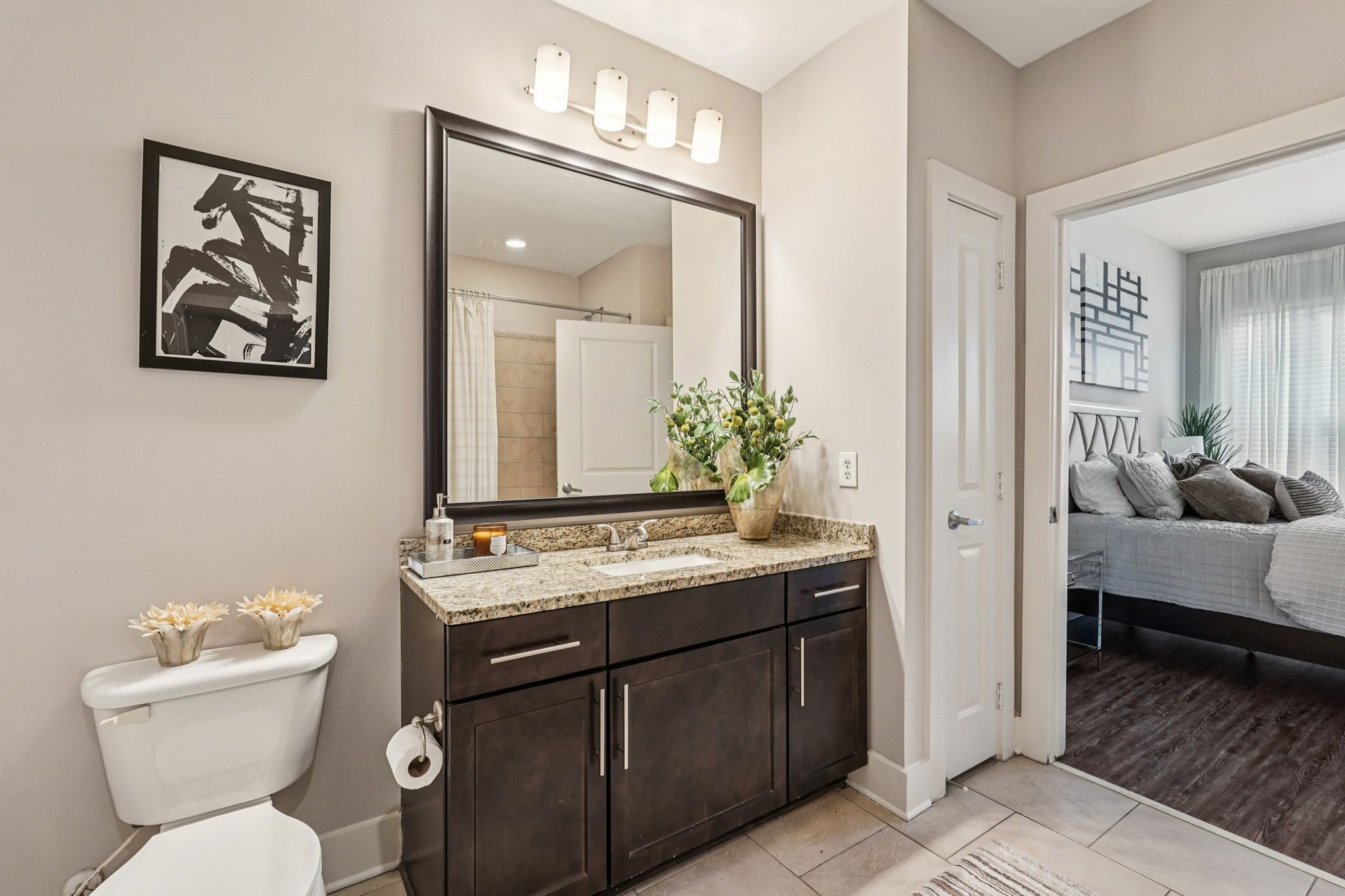 A bathroom with a white toilet, a large mirror, and a bedroom in the background.